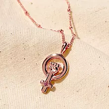 A rose gold necklace with a pink tourmaline stone on a piece of linen